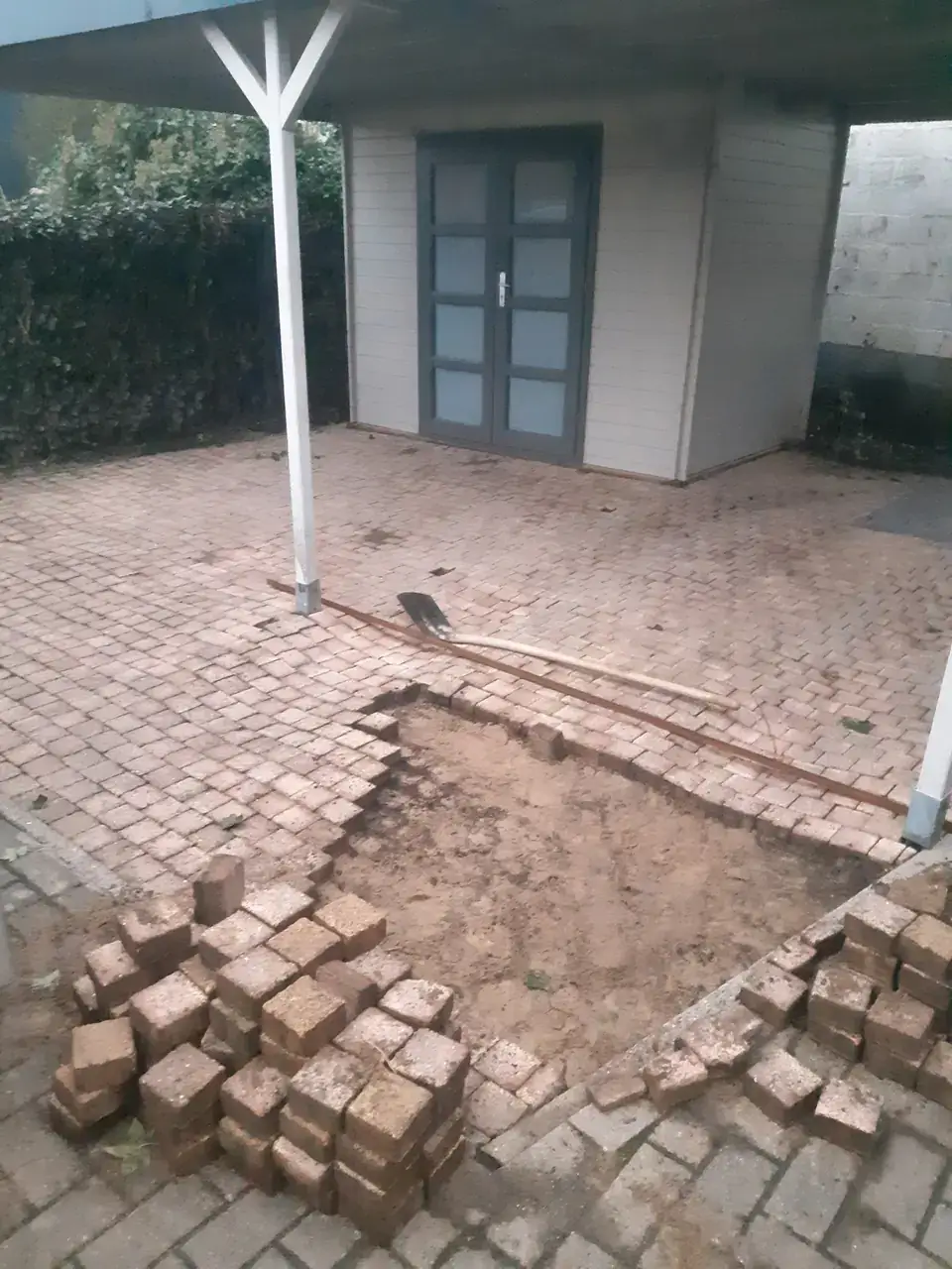 Verzakte klinkers onder een carport opgebroken om opnieuw te leggen