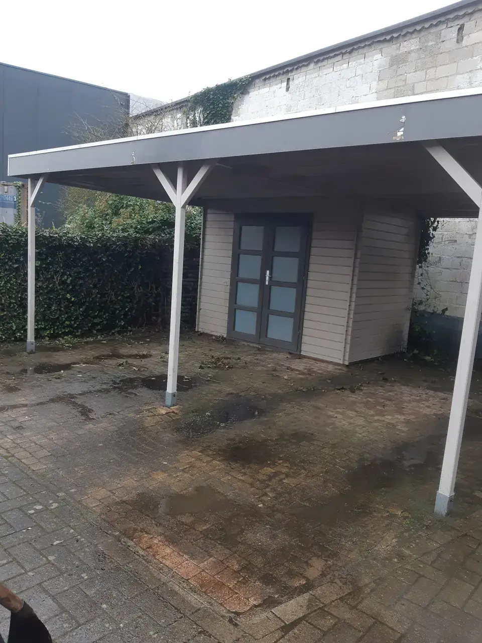 Vuile, verzakte klinkers met plassen onder een carport