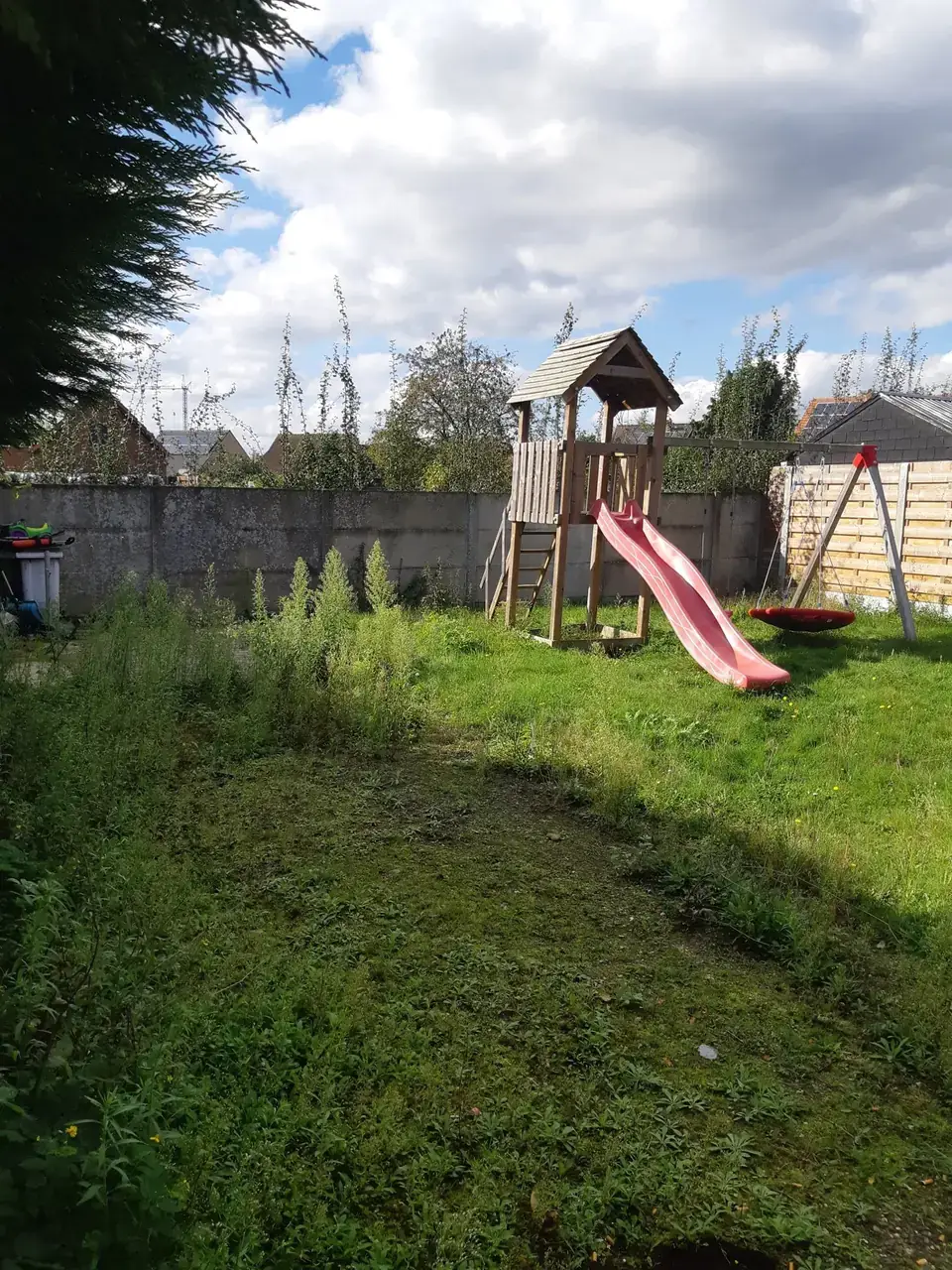 Tuin met speeltoren vol hoog onkruid