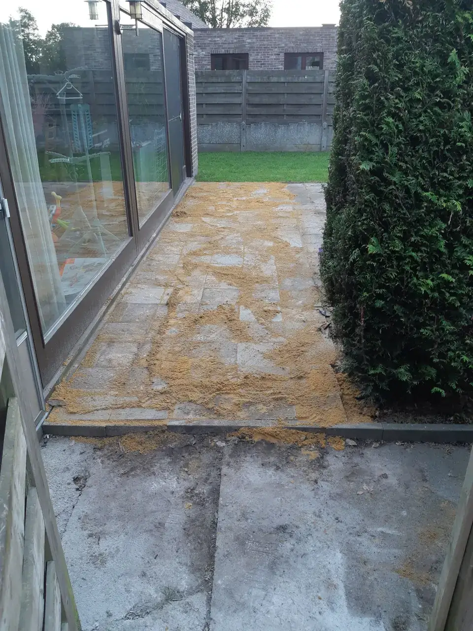 Voegzand wordt ingeborsteld op een terras langs een veranda